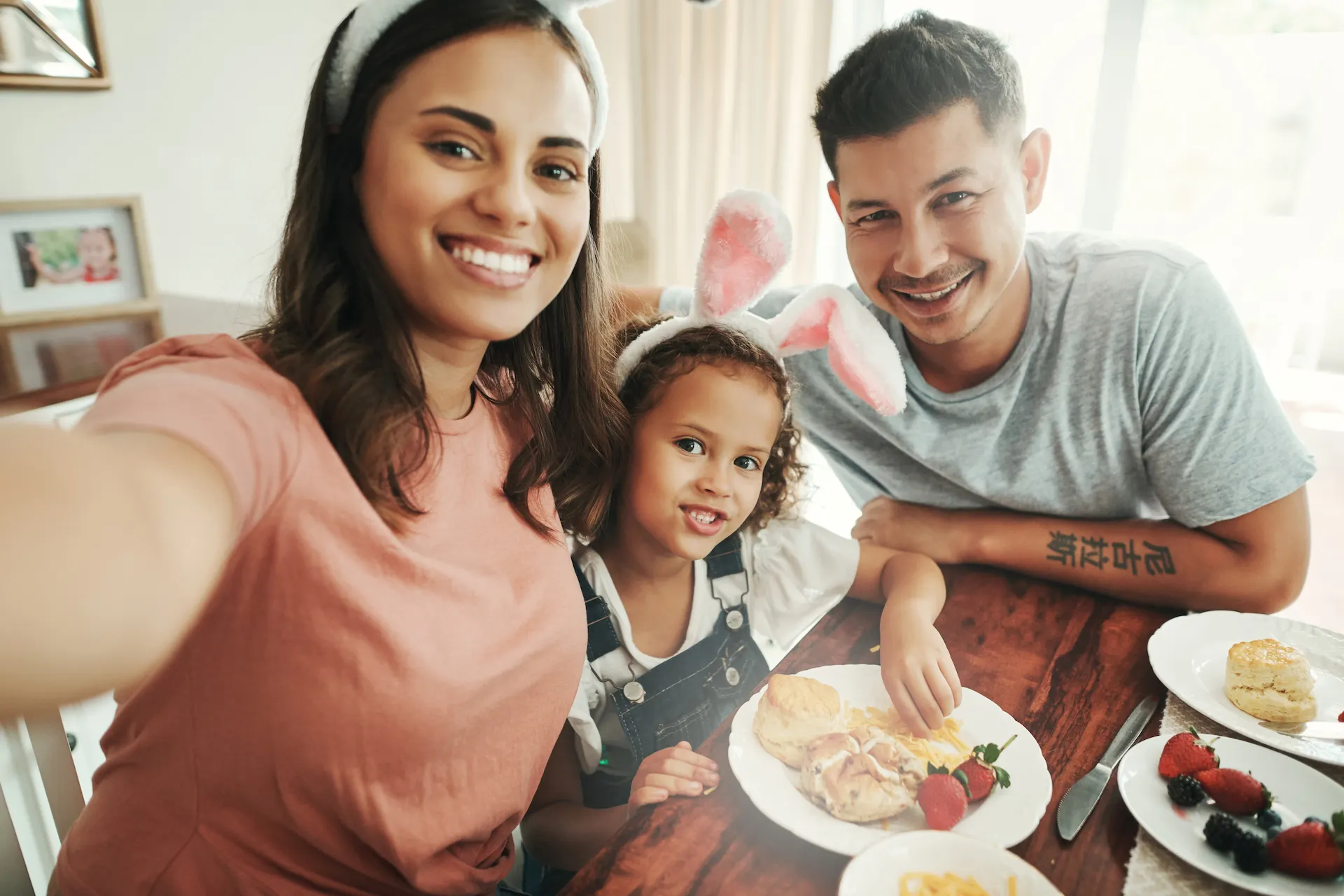 Familia sonriente disfrutando de un desayuno juntos en casa, con orejas de conejo decorativas en un ambiente cálido y familiar